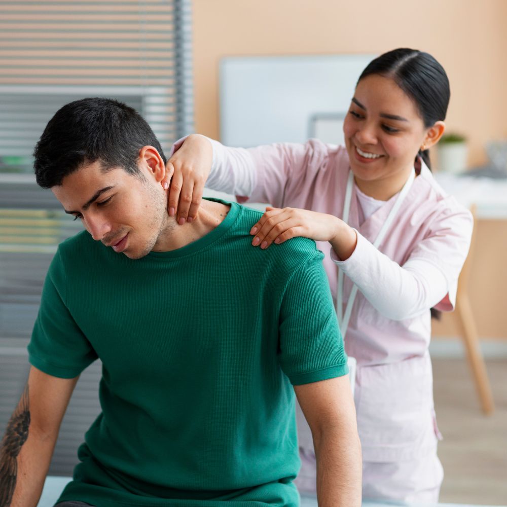 a smiling female physical therapist in a pink uniform providing neck therapy to a seated male patient in a green shirt, demonstrating care and expertise.